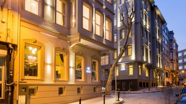 A row of multi-story buildings with illuminated windows, cobblestone street, and a parked car. - Nishant Boutique Hotels (Istanbul)