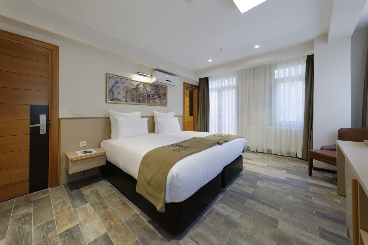 A hotel room with a large bed, a desk, a chair, a nightstand, and a painting on the wall.