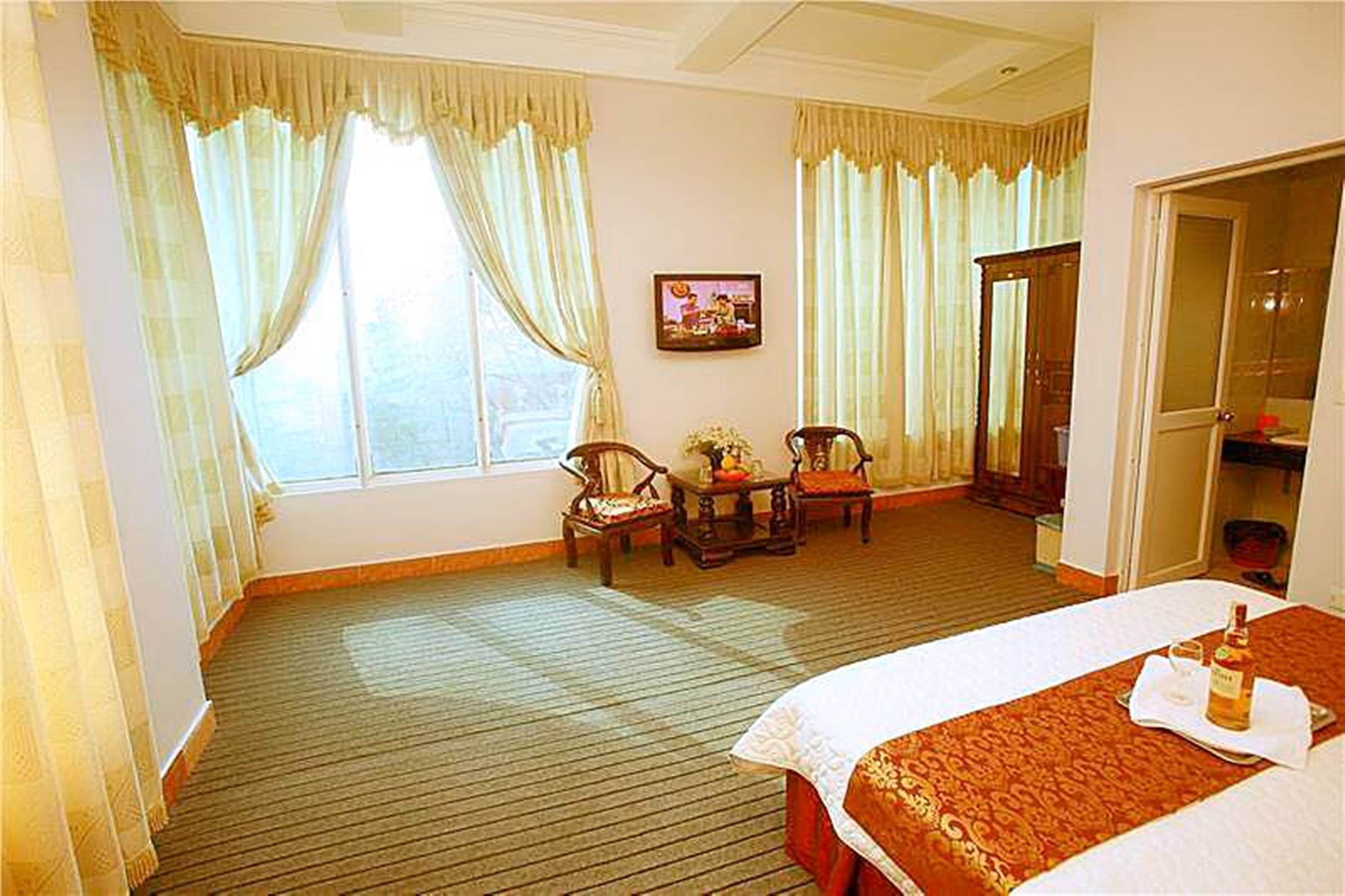 A hotel room with a large bed, a wooden floor, two chairs, a small table, and a mirror.