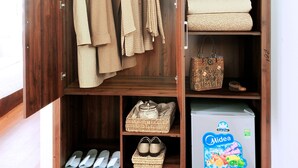 A wooden wardrobe with hanging clothes, folded blankets, and a storage box. - Van Giang Hotel (Hoa Lu)