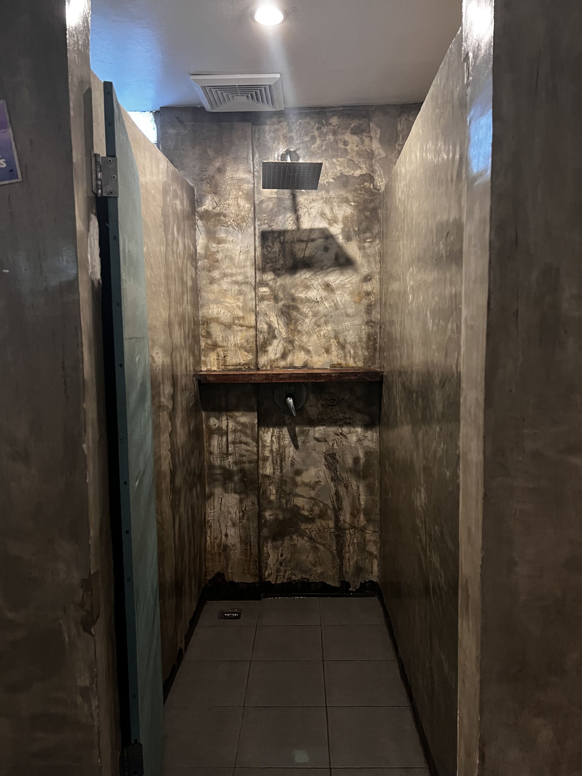 Un baño estrecho con baldosas, una pared de textura rugosa y un estante pequeño.