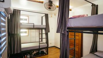 A dormitory room with bunk beds, a ceiling fan, and a window with curtains.