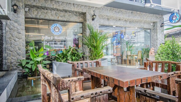 A rustic outdoor seating area with wooden tables and chairs, surrounded by greenery and a stone wall. - Casa Bella Phuket (Chalong)