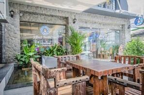 A rustic outdoor seating area with wooden tables and chairs, surrounded by greenery and a stone wall. - Casa Bella Phuket (Chalong)