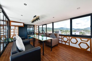 Un interior moderno con una mesa de vidrio, sofás negros y marrones, y vistas a la ciudad y a las montañas a través de amplios ventanales.