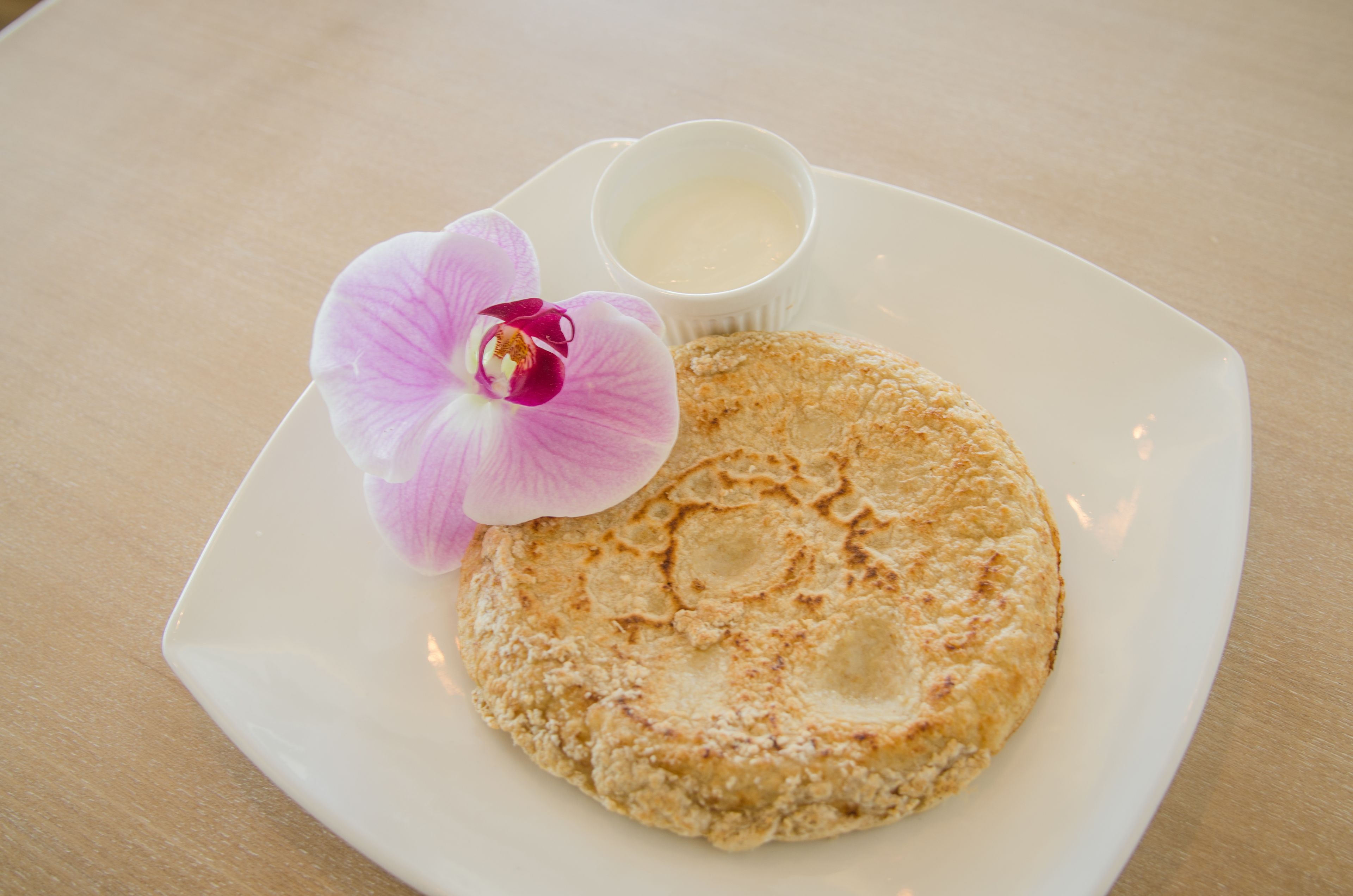 A plate with a crepe and a small cup of cream, accompanied by a pink orchid.