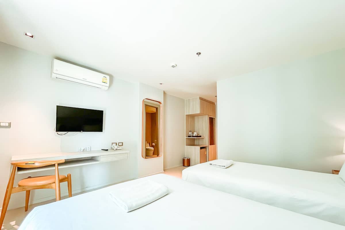 A hotel room with two beds, a desk, a chair, a TV, and a bathroom with a mirror and toilet.