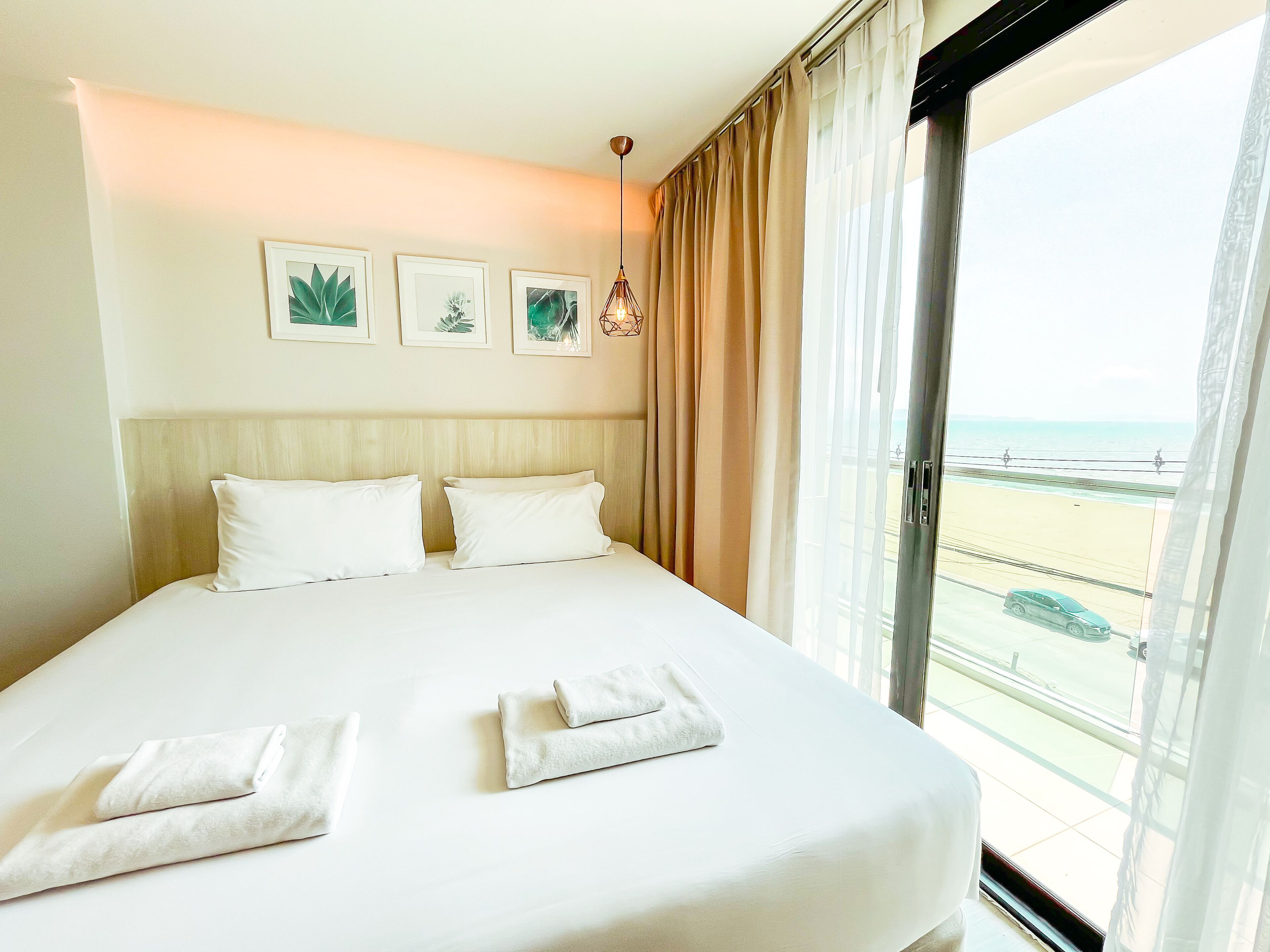 A hotel room with a large bed, beige curtains, and a view of the beach.