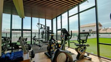 Een sportschool met trainingsapparatuur, grote ramen en uitzicht op een gebouw.