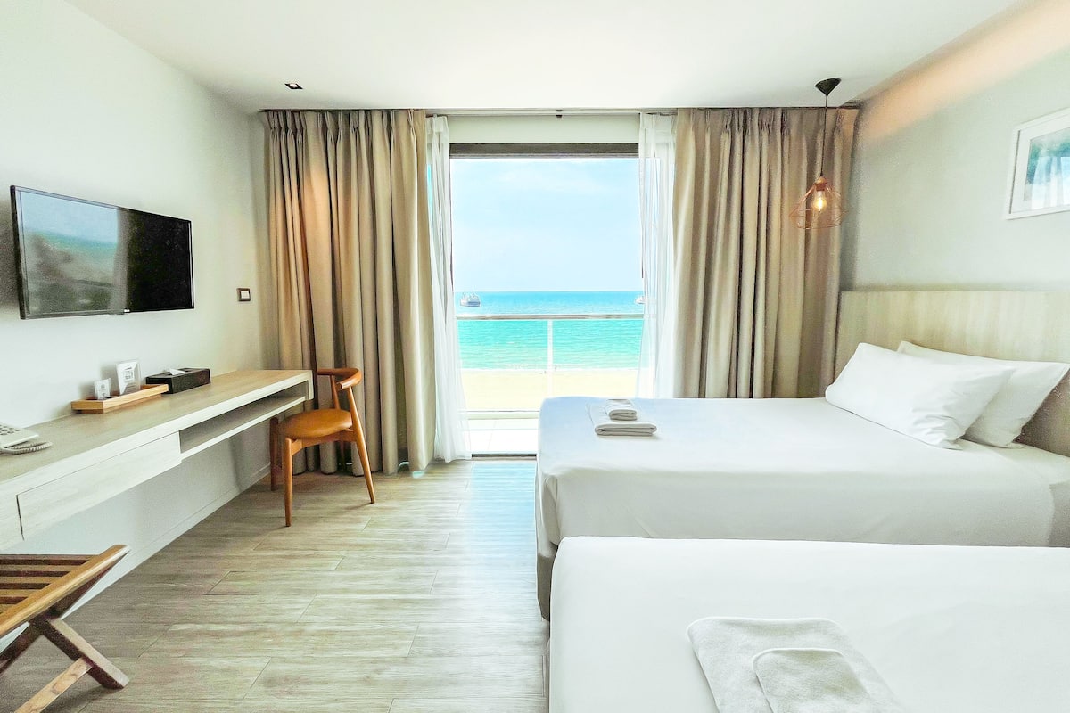 A hotel room with a bed, a desk, a chair, a TV, and a view of the ocean.