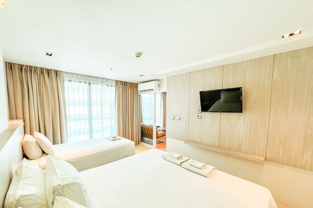 A hotel room with two beds, a TV on the wall, and a view of the outdoors through the window.