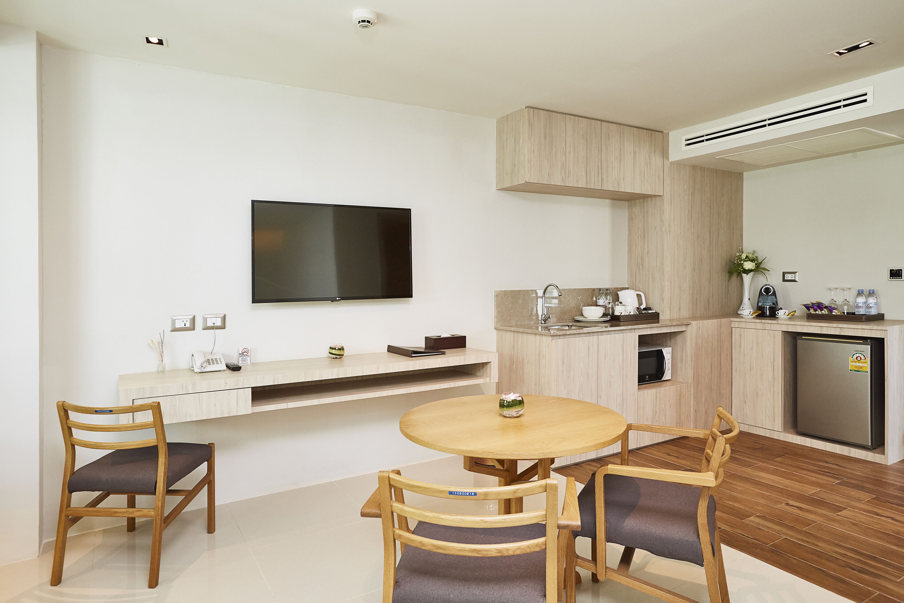 A modern kitchen with a built-in oven, microwave, and refrigerator. There is a wooden dining table with chairs and a flat-screen TV mounted on the wall.