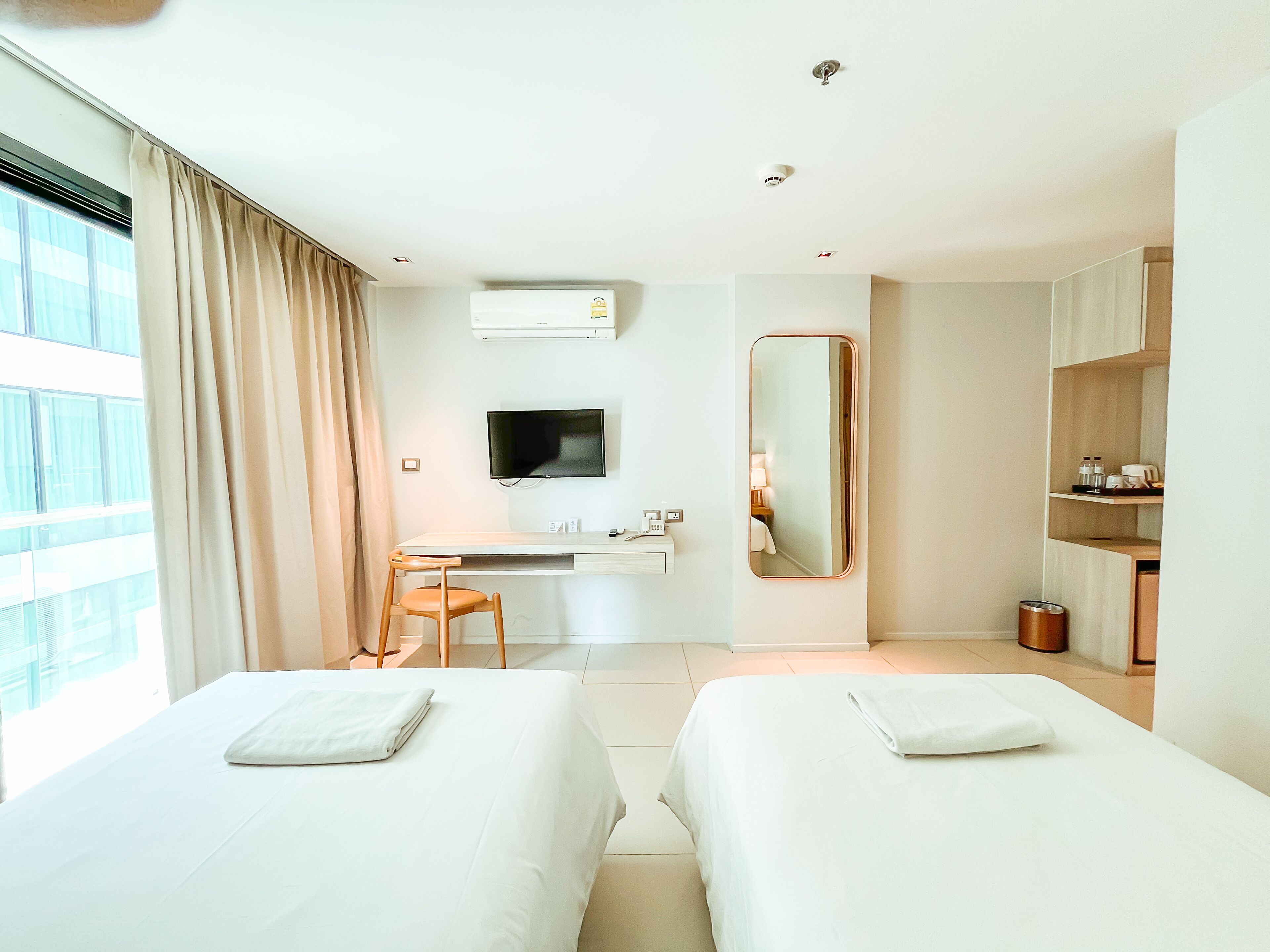 A hotel room with two beds, a desk, a TV, and a bathroom.