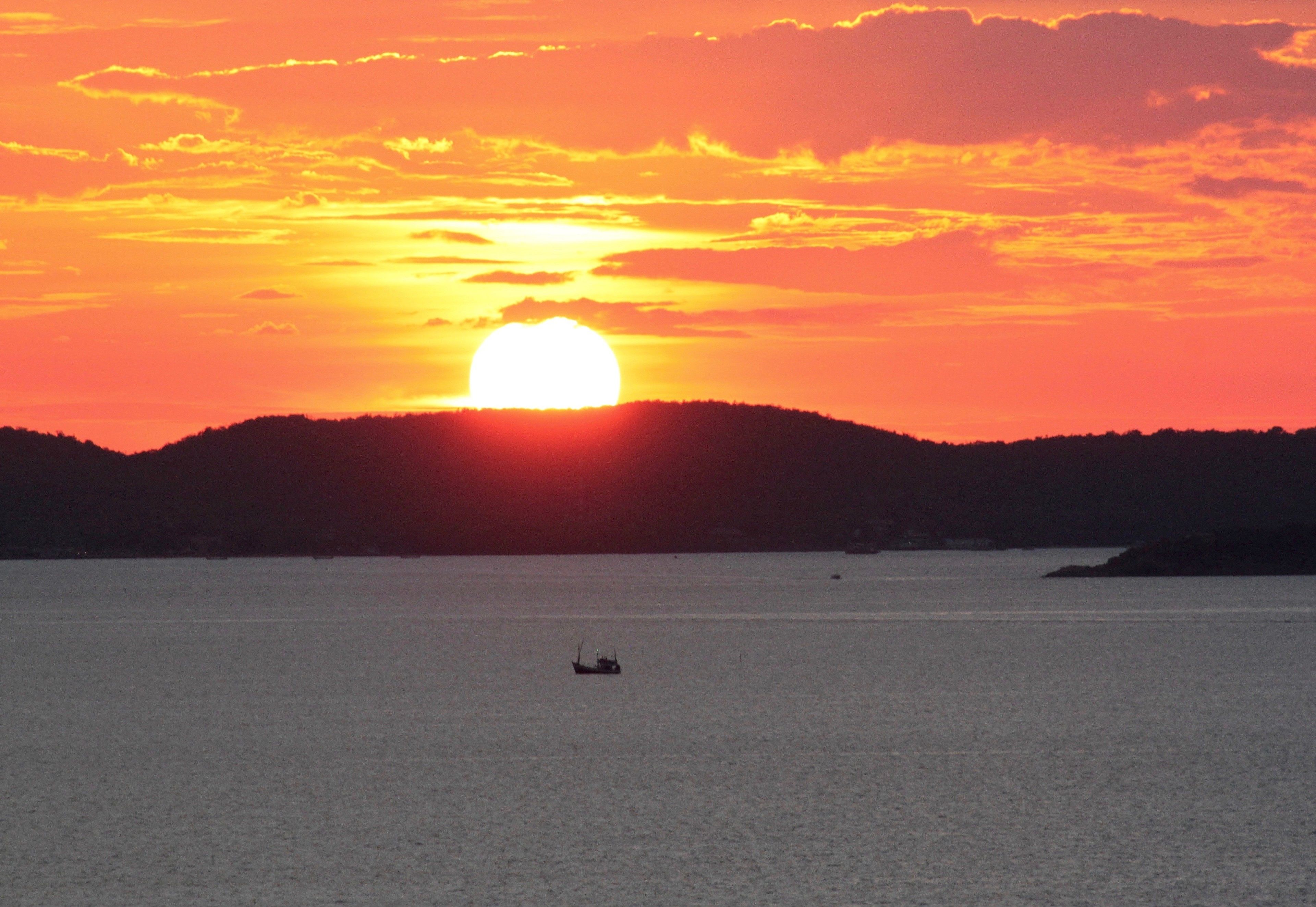 Ein Sonnenuntergang über einem ruhigen Meer mit einem Boot in der Ferne.