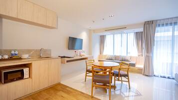 A modern kitchen with a microwave, a dining area with a round table and chairs, a flat-screen TV mounted on the wall, and a large window with curtains.