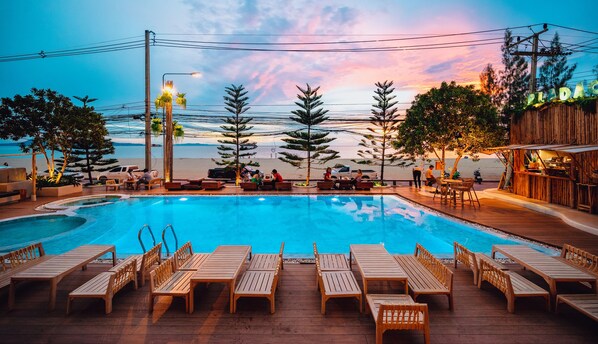 A poolside area with wooden loungers, a pool, and a view of the beach. - Zand Morada Pattaya (Pattaya)