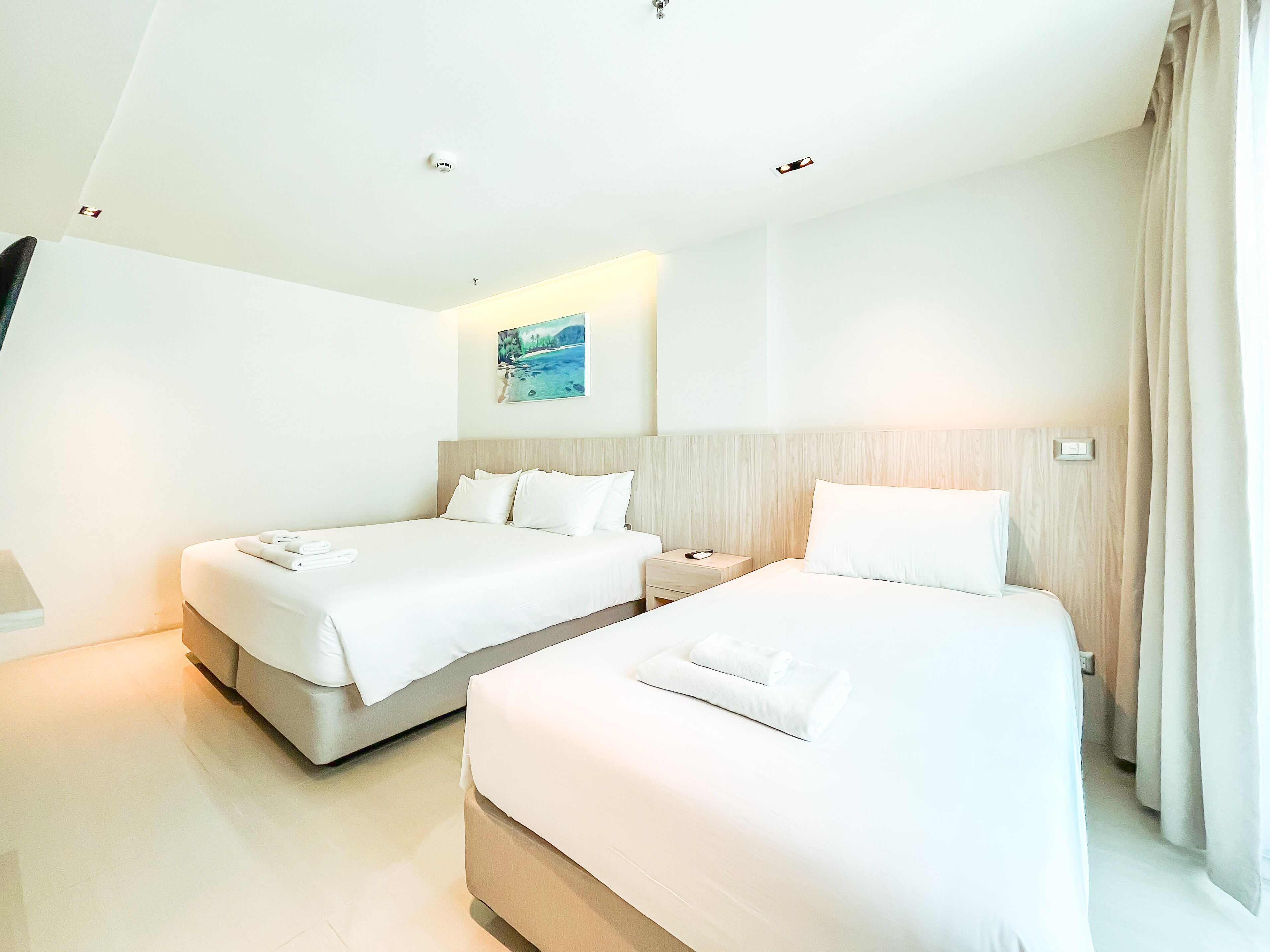 Una moderna camera d'albergo con due letti, un comodino, un quadro appeso al muro e una lampada a soffitto.