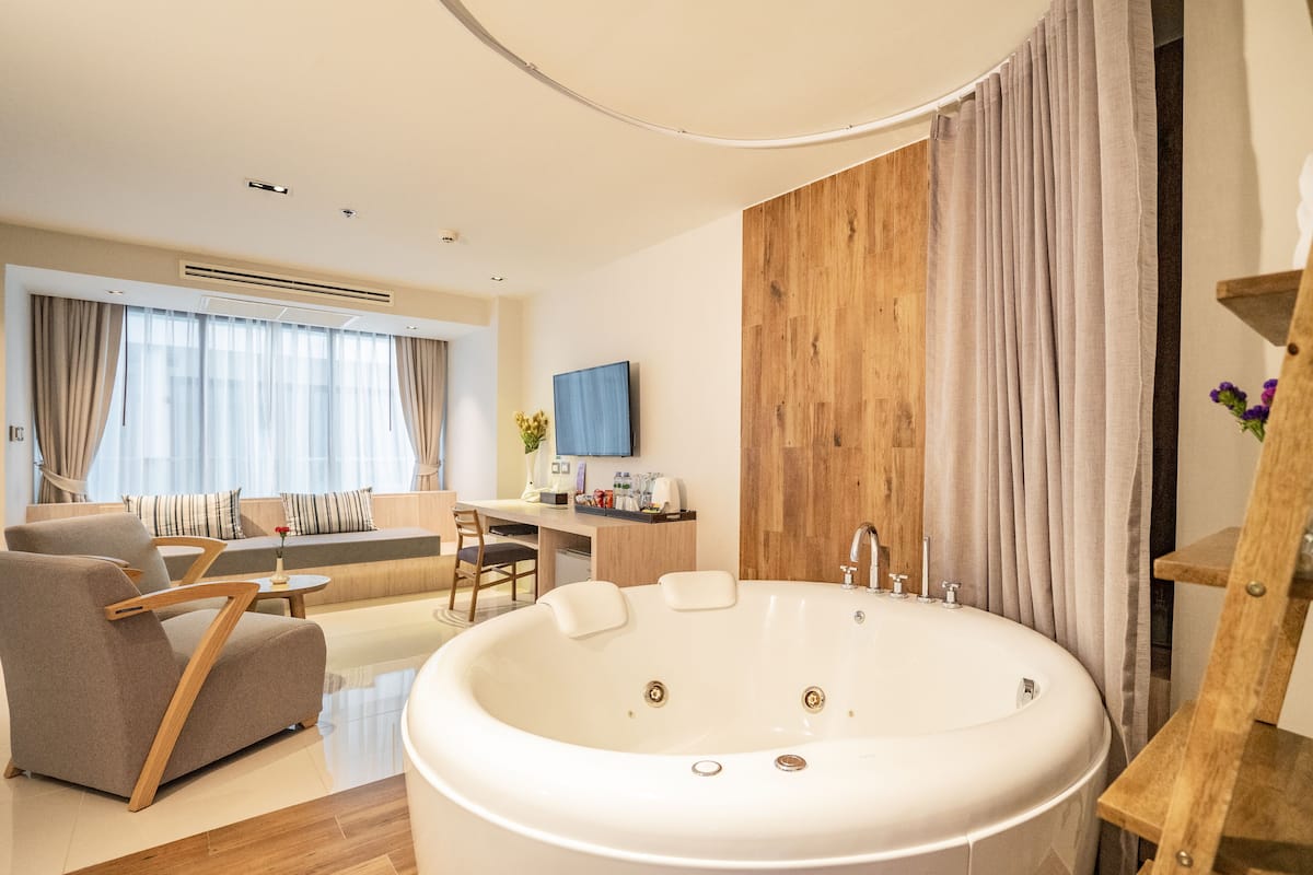 A modern bathroom with a large bathtub, a wooden vanity, and a seating area with a sofa and chairs.
