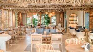 Amplia sala de estar moderna con muebles de madera, un área de estar central y grandes ventanales que permiten la entrada de luz natural.