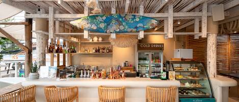 A bar area with wicker chairs, a display case of desserts, and a sign for 'COLD DRINKS'.
