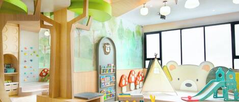 Uma sala de jogos infantil com uma estrutura de recreação de madeira, prateleiras com brinquedos e uma grande janela com vista para árvores.