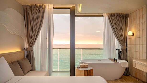 Una habitación de hotel moderna con una cama grande, una bañera y un balcón con vistas al mar.