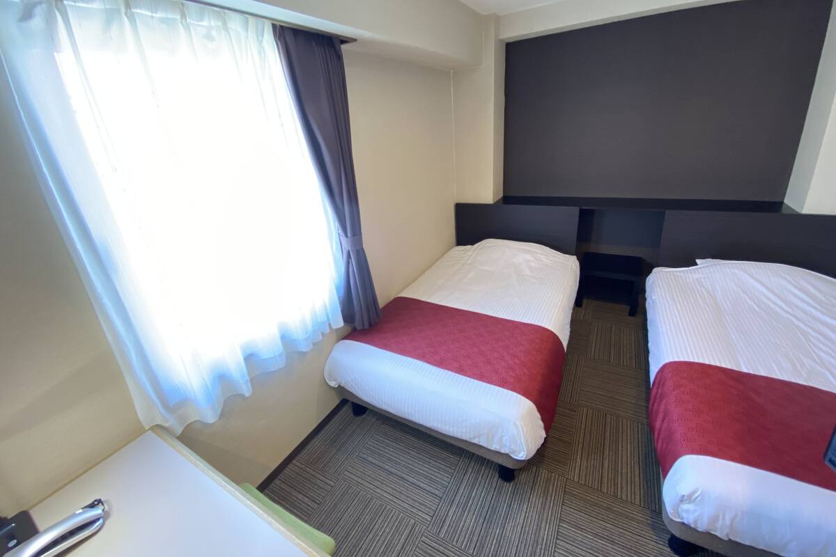 A hotel room with two beds, a desk, and a large window with curtains.