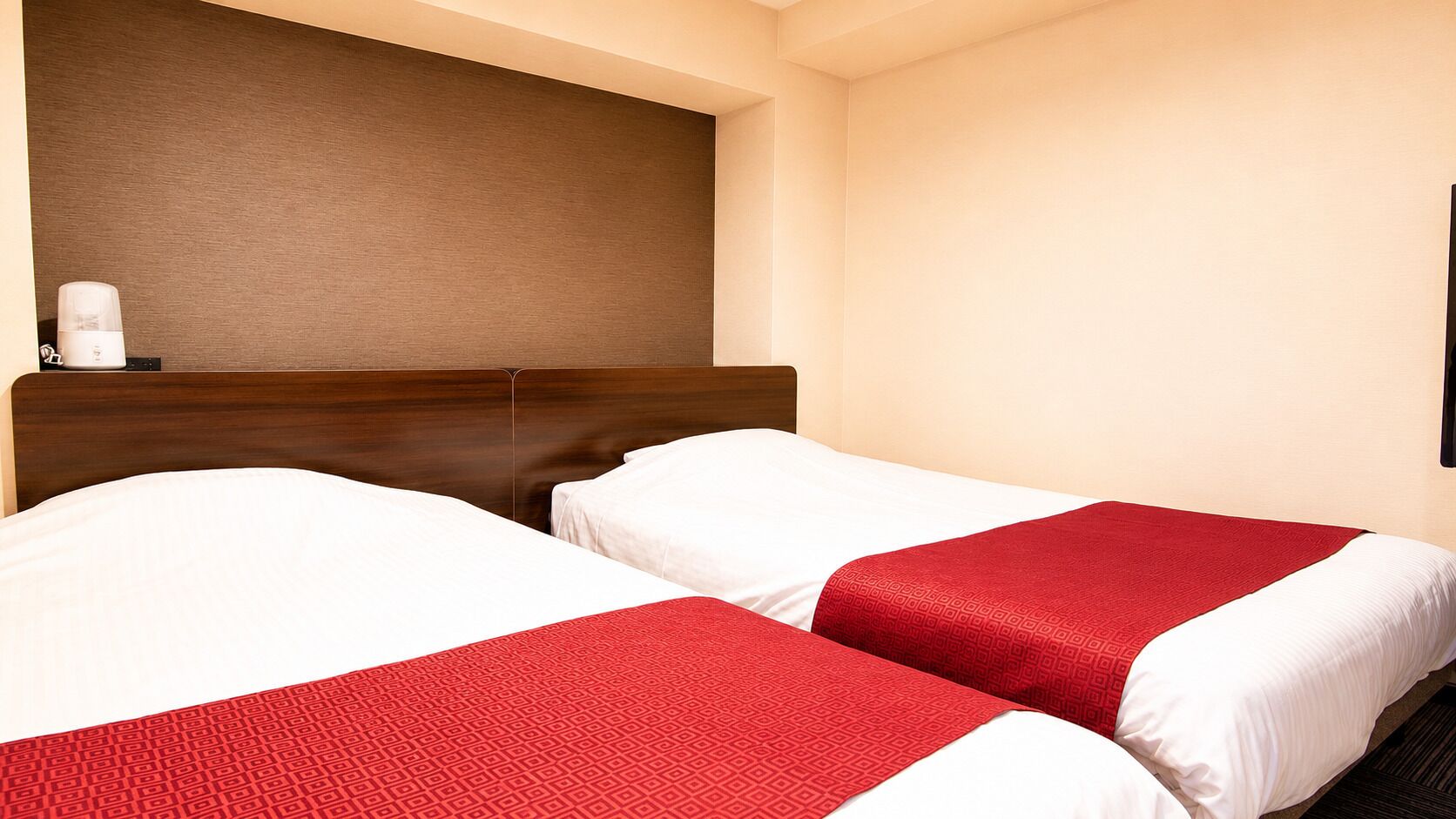 A hotel room with two beds, a wooden headboard, and a wall-mounted coffee maker.