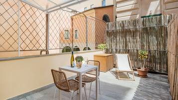 A balcony with a table, chairs, a potted plant, and a hanging plant.