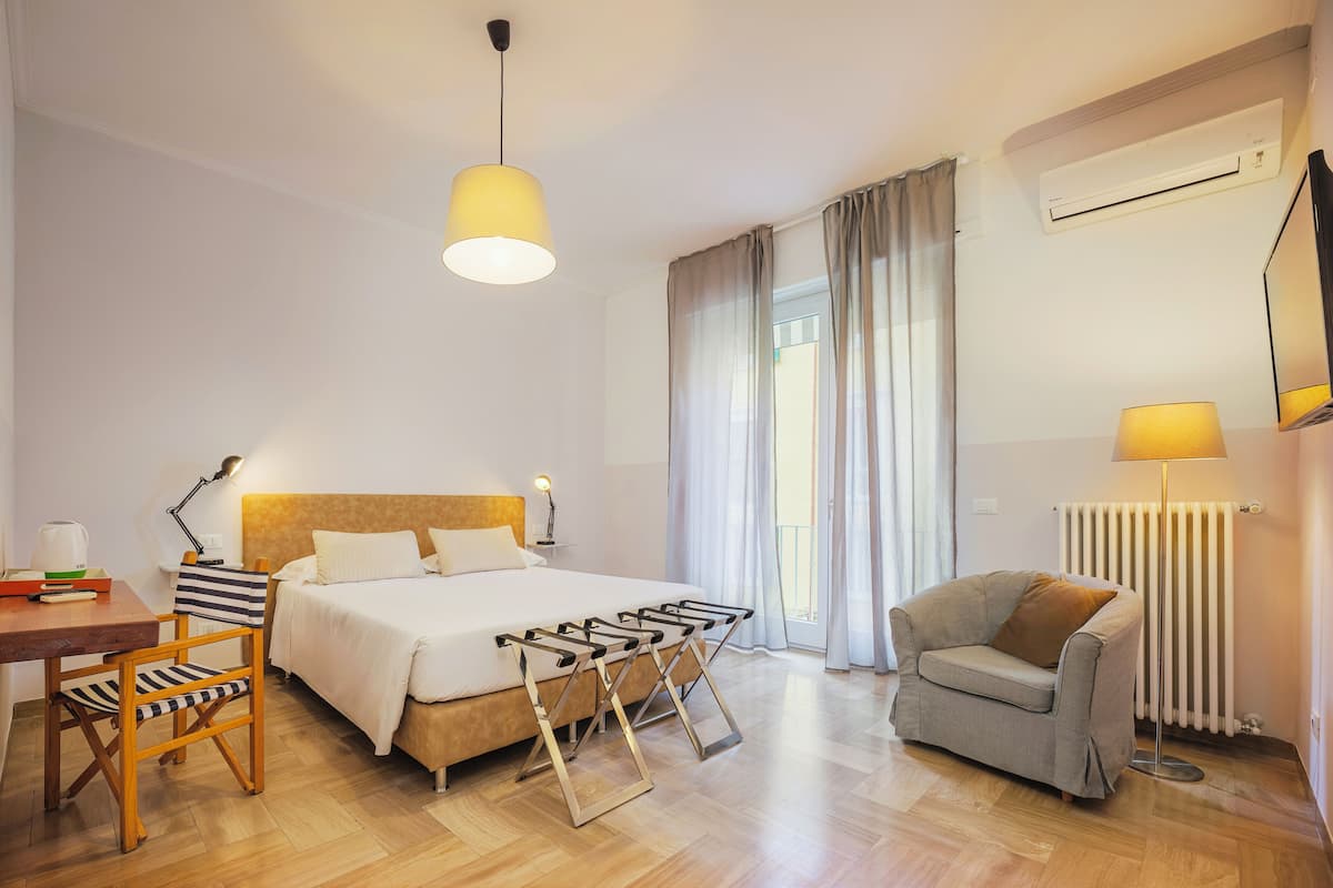 Una habitación de hotel con cama, mesita de noche, lámpara, silla y un radiador.