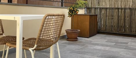 Un patio al aire libre con una mesa blanca y sillas de mimbre, una planta en maceta y una cerca de madera.