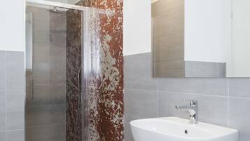 Un baño moderno con cabina de ducha de vidrio, un lavamanos blanco y un espejo grande.