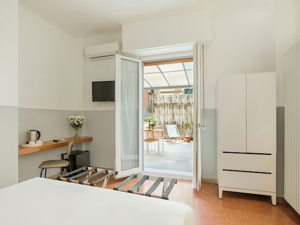 A modern hotel room with a bed, a desk with a chair, a TV mounted on the wall, and a sliding glass door leading to an outdoor area with a table and chairs. - La Casa delle Acciughe (La Spezia)