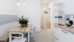 Una cocina compacta con una mesa de madera, sillas blancas, una planta en maceta y una cafetera.