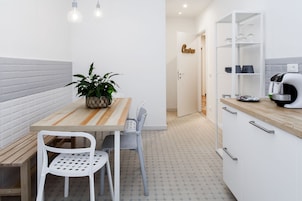 Una cocina compacta con una mesa de madera, sillas blancas, una planta en maceta y una cafetera.