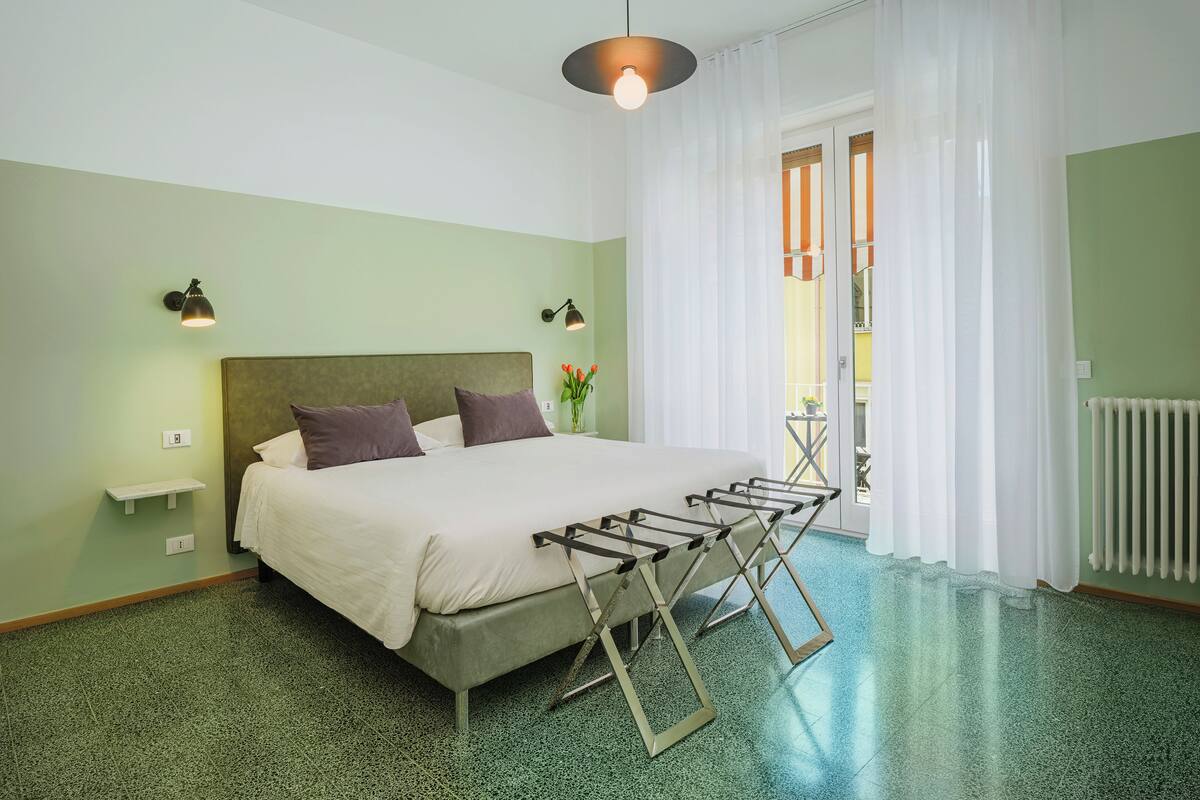 Un dormitorio ordenado con cama, lámparas de noche, un radiador y un tendedero.