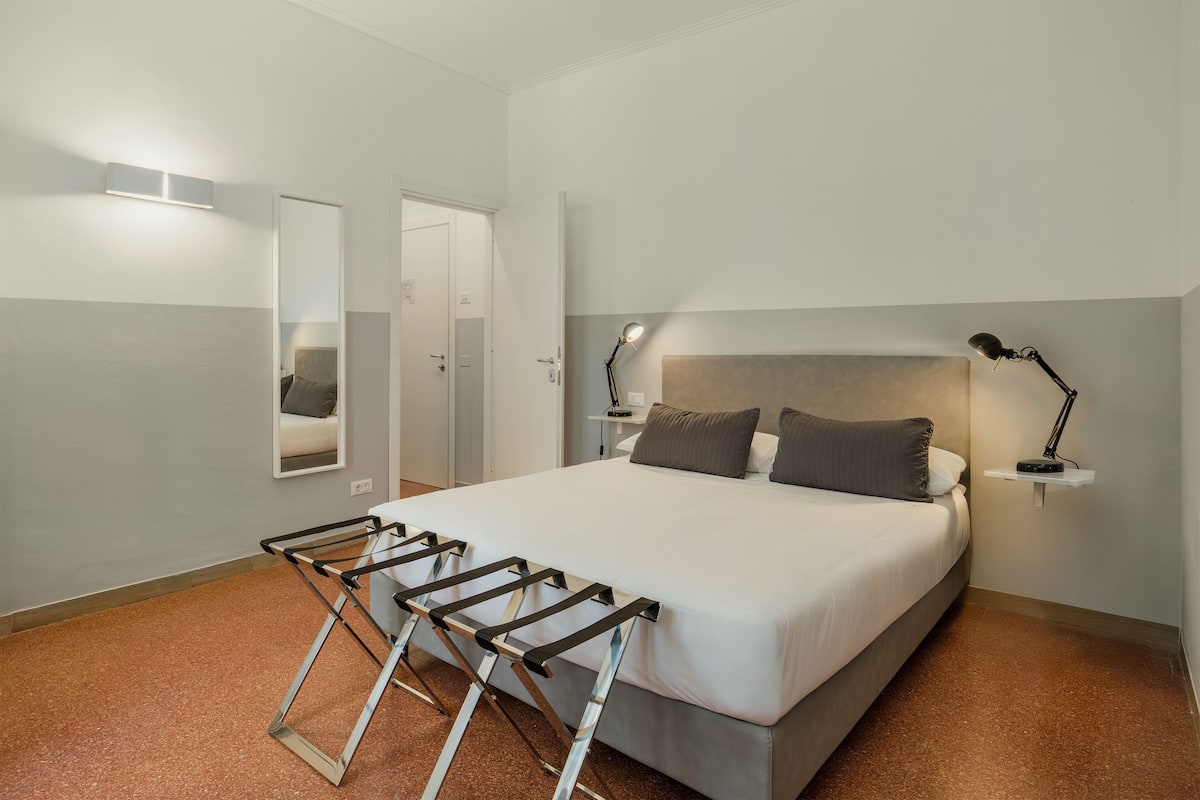 Un dormitorio con una cama, dos lámparas de noche, un espejo y una puerta.