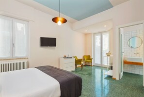 A hotel room with a bed, a desk with a flat-screen TV, a chair, a small shelf, and a bathroom with a sink and mirror. - La Casa delle Acciughe (La Spezia)