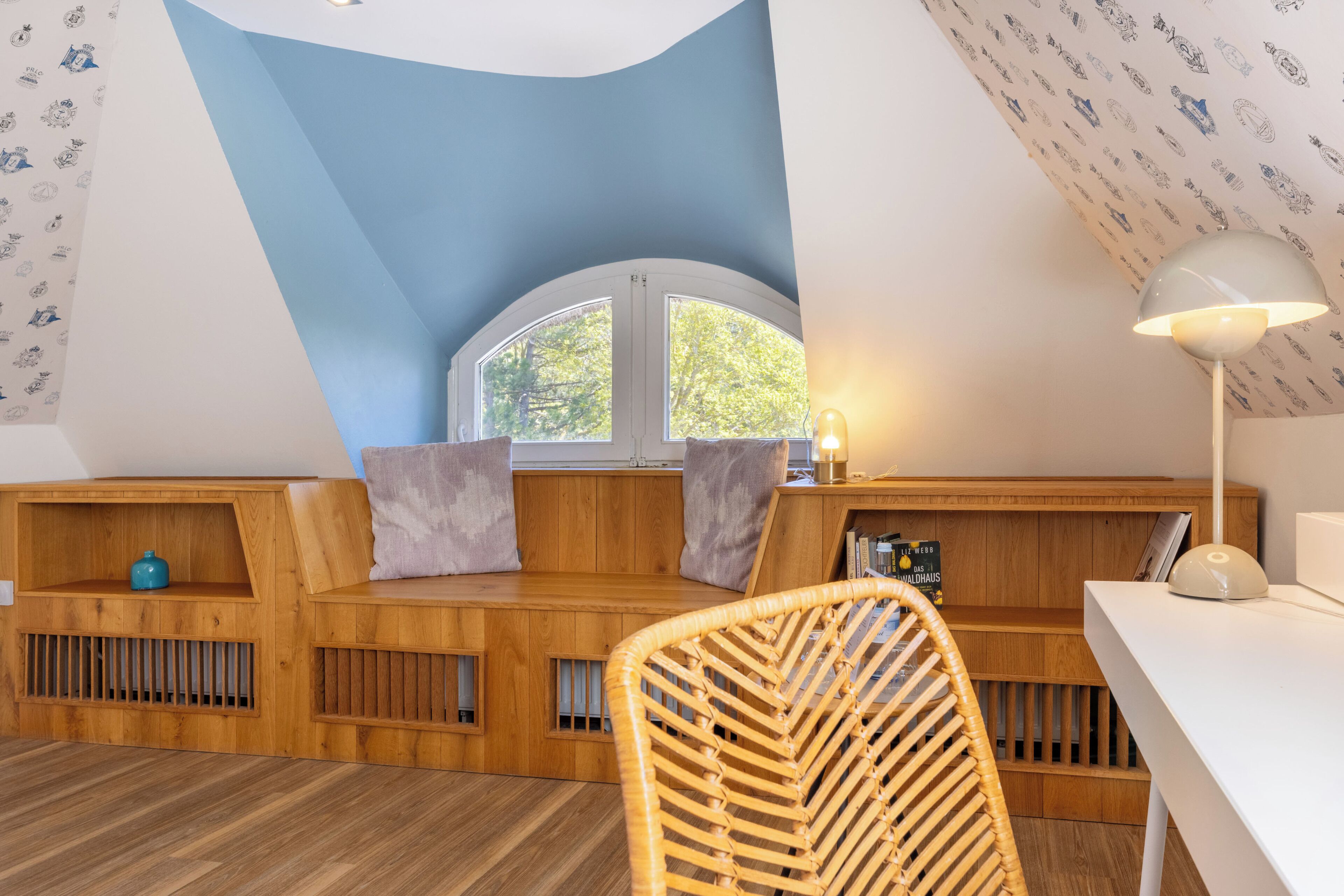Un dormitorio acogedor en el ático con ventana integrada, muebles de madera y una silla de ratán.