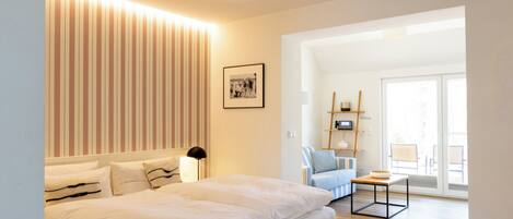 Een moderne hotelkamer met een groot bed, nachtkastje, lamp, een ingelijst schilderij aan de muur en uitzicht op het buitengebied.