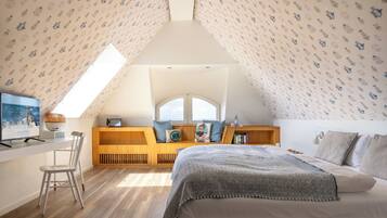 Un dormitorio con techo inclinado, una cama, un escritorio, una silla y una ventana con vistas.