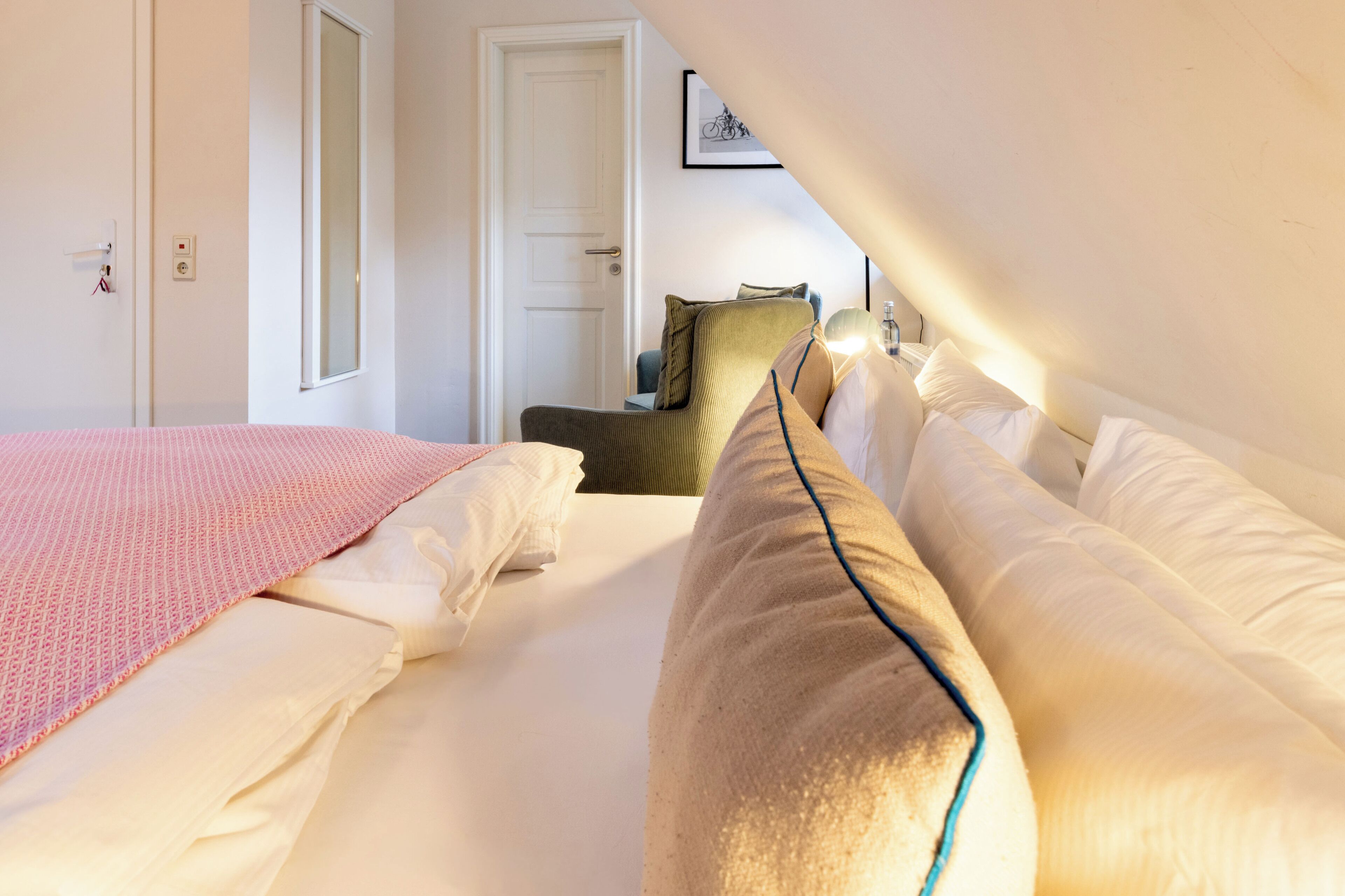 A bedroom with a bed, pillows, a bedside table, a chair, and a door.