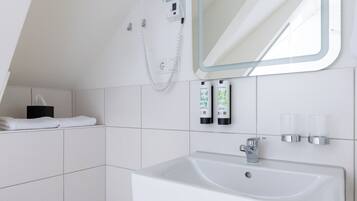 A modern bathroom with a white sink, a handheld showerhead, and toiletries on the wall.