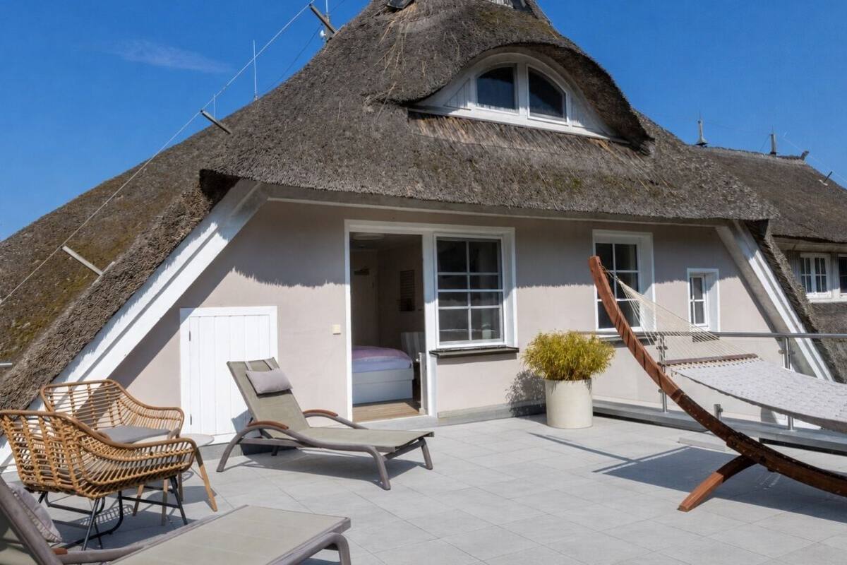 A thatched-roof house with a balcony, wicker furniture, and a potted plant.