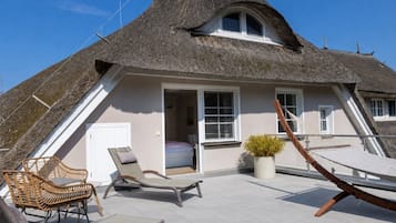 Ein Haus mit einem Strohdach, einem Balkon, Korbmöbeln und einem Blumentopf.