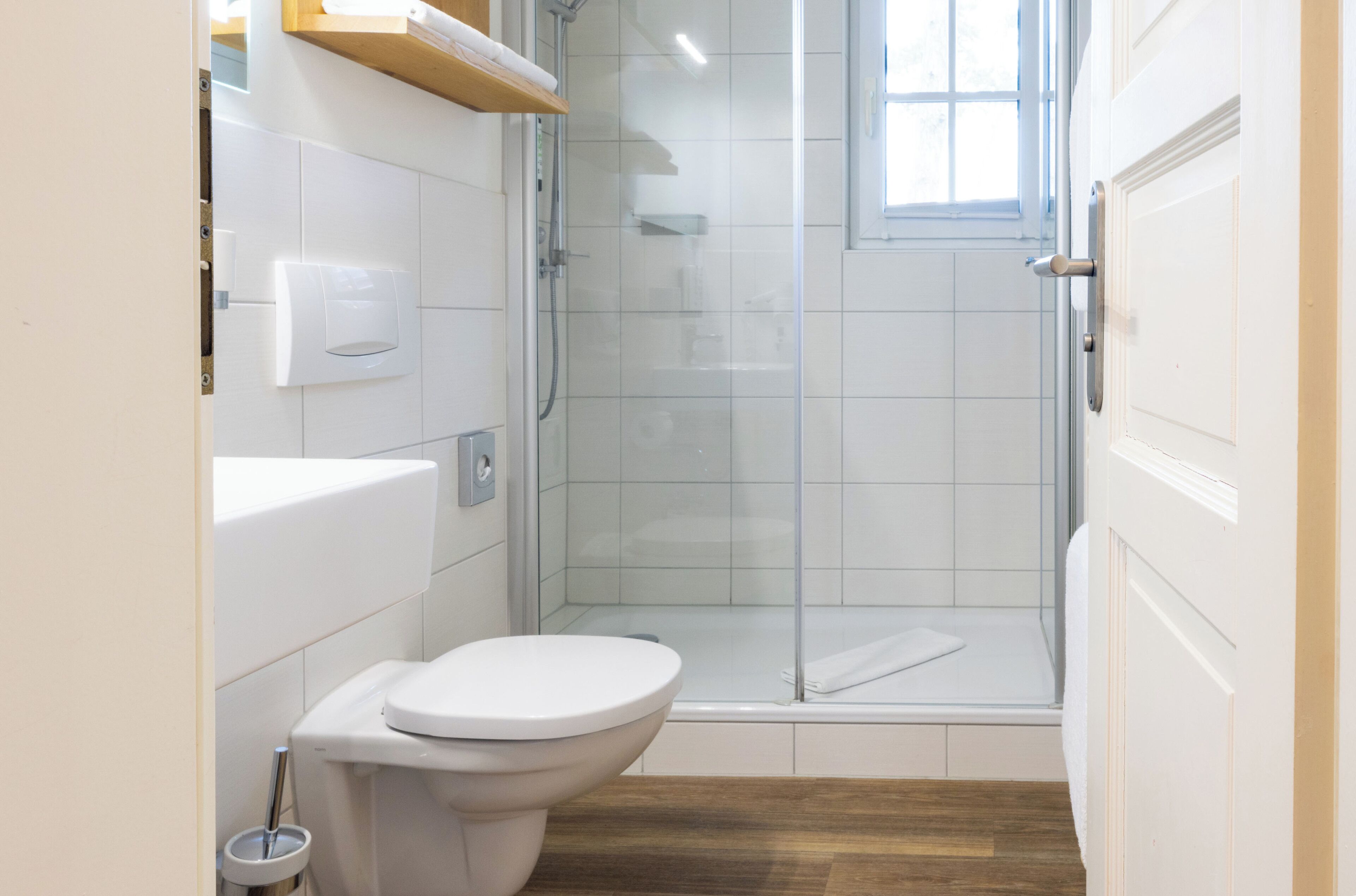 A modern bathroom with a toilet, a glass-enclosed shower, and a wooden floor.