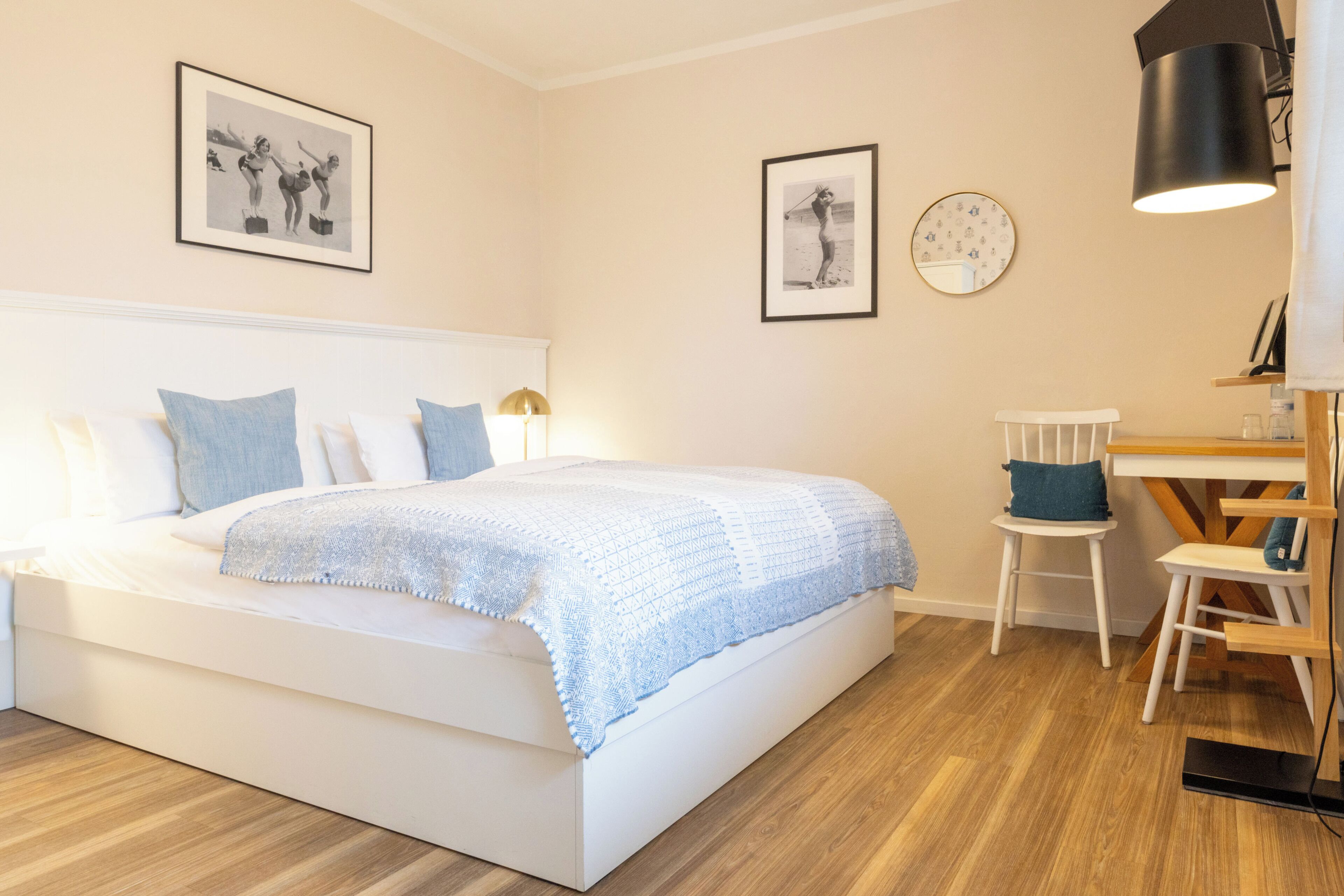 A bedroom with a bed, a desk, and two framed pictures on the wall.
