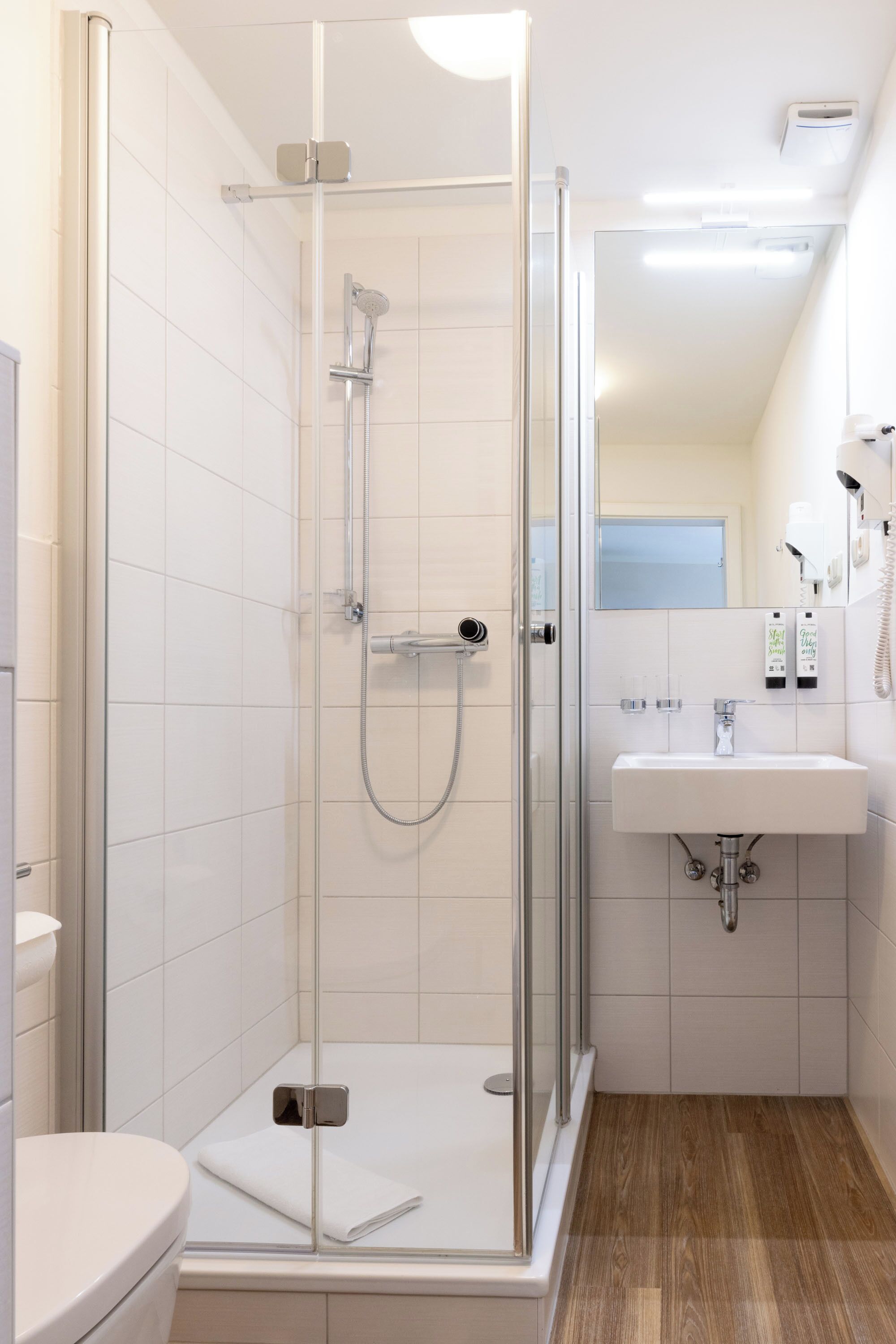 A modern bathroom with a glass-enclosed shower, a white sink, and a wooden floor.