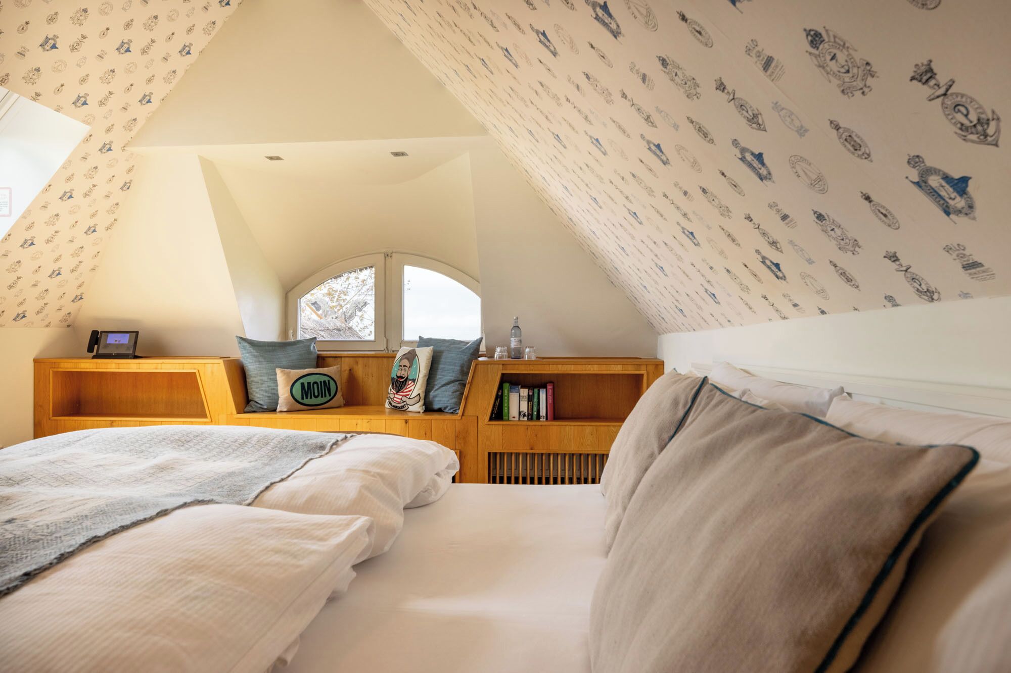 A cozy attic bedroom with two beds, a wooden bench with a mirror, and a bookshelf.