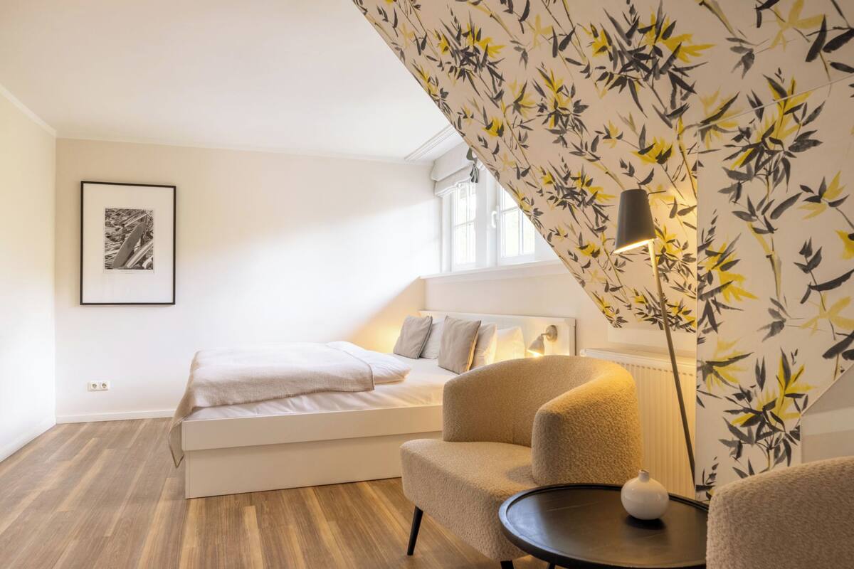 A bedroom with a bed, a chair, a lamp, and a picture on the wall.